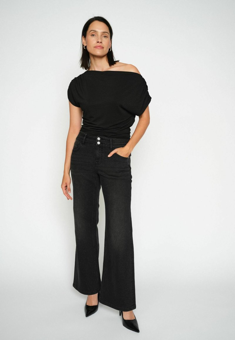Top nero off-the-shoulder abbinato a jeans neri a vita alta e a gamba larga. Caratteristiche notevoli includono tre bottoni frontali e una texture denim liscia.