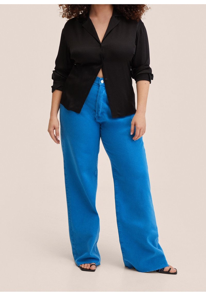 Chemise noire en satin à boutons avec manches retroussées, associée à un jean en denim bleu vif à jambes larges. Texture lisse et couleurs contrastées.