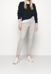 Jeans ajustados de color gris claro con ligero desgastado, combinados con un suéter corto azul marino y zapatillas blancas de plataforma. Textura suave, diseño ceñido.