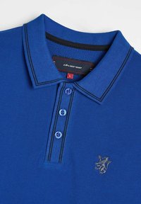 Niebieska koszulka polo z teksturowanej tkaniny, zapięcie na trzy guziki, kontrastowy ciemny kołnierzyk oraz detale ściegowe, a także haftowane logo na piersi.