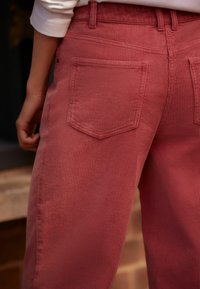 Kalhoty z bavlněného manšestru v jemné růžové barvě, s vertikálním žebrováním, dvěma zadními kapsami a uvolněným střihem nohavic.