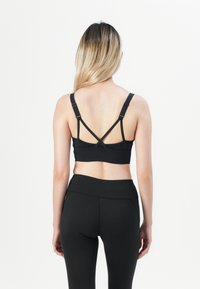 Black sport bra with adjustable straps featuring a racerback design. Smooth fabric with a fitted silhouette and minimal seams. Black leggings visible.