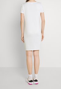 Biała bawełniana sukienka t-shirtowa z krótkimi rękawkami, okrągłym dekoltem i luźnym krojem, zestawiona z białymi i czarnymi sportowymi butami.