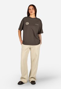 Czarnogranatowa bawełniana koszulka z okrągłym dekoltem, krótkimi rękawami i logo na lewej piersi. W zestawieniu z jasnobeżowymi, strukturalnymi spodniami o szerokich nogawkach.