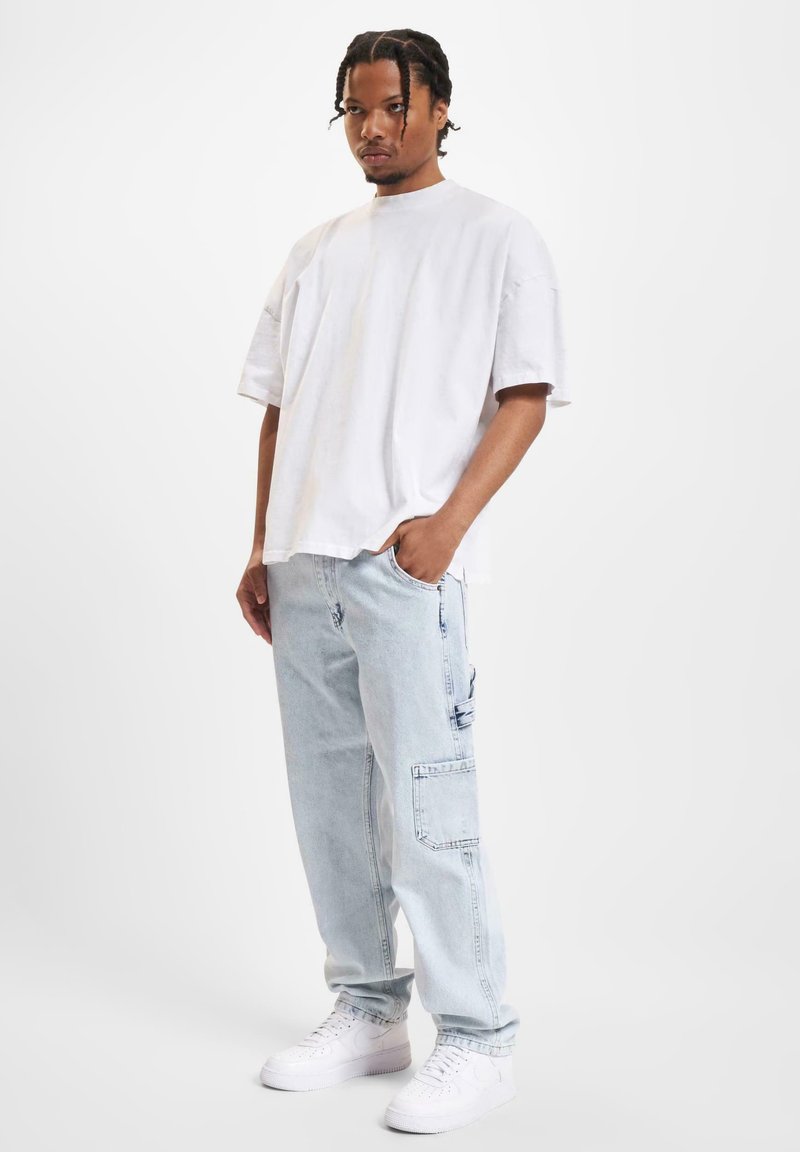 Hvit oversized t-skjorte, lyseblå denim cargobukser med sidelommer, og hvite joggesko. Enkel, avslappet passform, glatt tekstur.