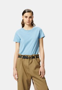 T-shirt di cotone azzurro chiaro con colletto a girocollo e maniche corte, caratterizzato da un piccolo logo ricamato. Abbinate a pantaloni beige a vita alta.
