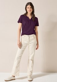 Maglietta viola a maniche corte con scollo a V abbinata a jeans dritti crema e sneakers beige. Tessuto morbido con vestibilità rilassata.