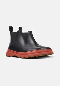 Svarta läder Chelsea-boots med en röd gummisula, med dragflikar och en strukturerad yttersula för grepp. Slät yta, stilren design.
