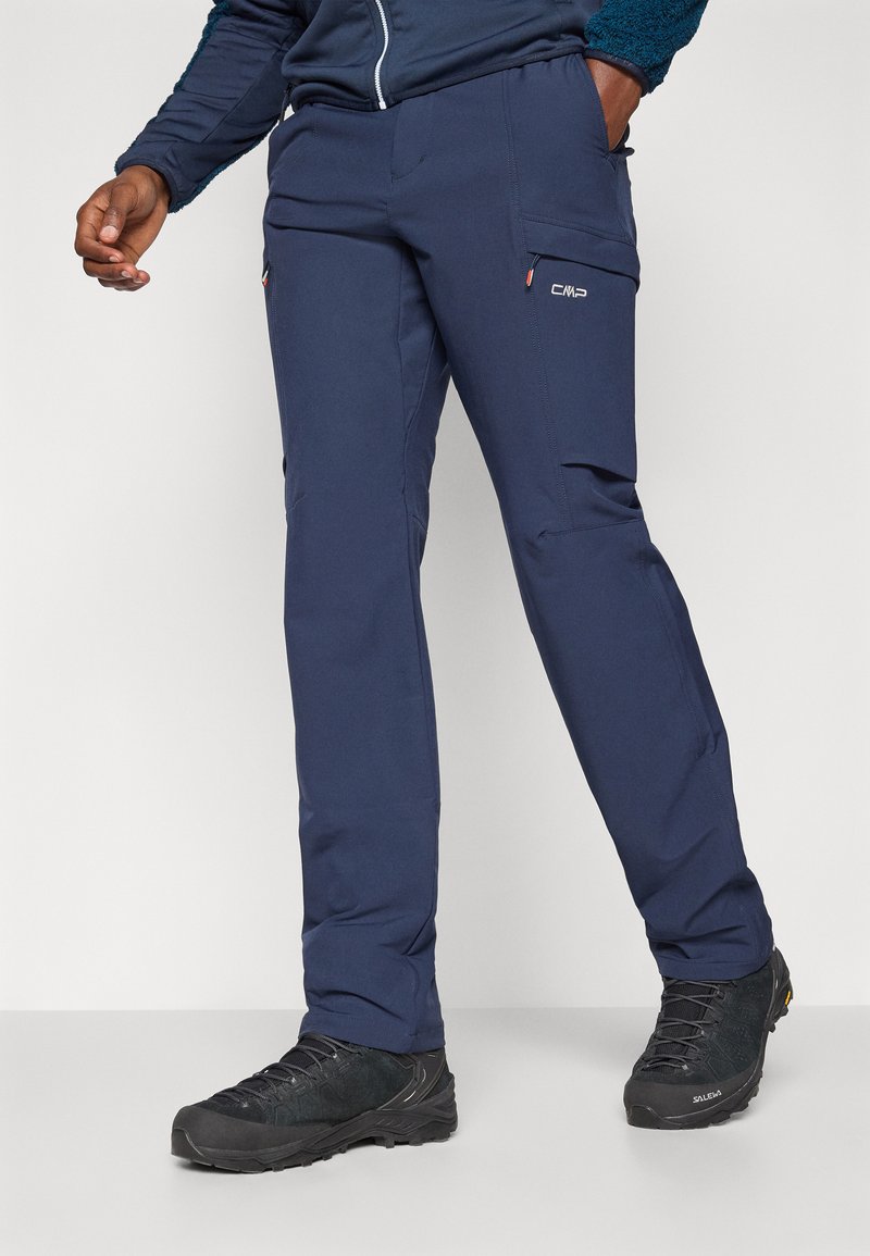 Granatowe spodnie outdoorowe wykonane z elastycznego, trwałego materiału, z bocznymi kieszeniami i dopasowanym krojem. W połączeniu z czarnymi butami trekkingowymi o fakturowanej powierzchni.