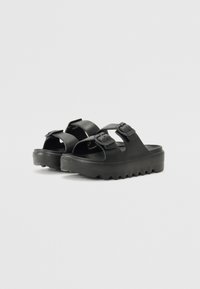 Black sandals made of rubber, featuring two adjustable straps and a chunky, serrated sole for traction. Smooth texture with no patterns.