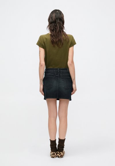 Haut à manches courtes couleur vert olive associé à une minijupe en denim foncé, dotée de poches arrière et de coutures minimalistes, complété par des chaussures à imprimé animal.