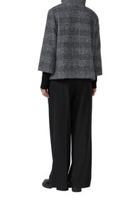 Kurtka z mieszanki wełny w kratkę, z wysokim kołnierzem, szerokimi rękawami oraz czarnymi luźnymi spodniami. Widać czarne masywne obuwie.