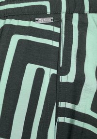 Tkanina marki Cecil z geometrycznym wzorem w czerni i miętowej zieleni. Posiada srebrną metkę z logo oraz gładką teksturę.