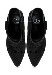 Botines negros con superficie texturizada, puntera puntiaguda y paneles laterales elásticos. Logotipo "CG" visible en el forro interior.
