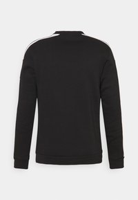Sweat-shirt à manches longues noir avec des rayures blanches le long des coutures des épaules, vu de dos sur un fond uni.