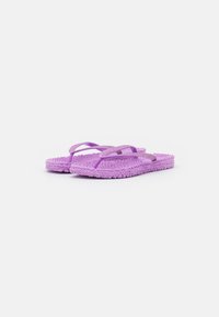 Violet flip-flopit, joissa on teksturoitu pohja ja kimaltelevat hihnat, joissa on kudottu muotoilu ja tasainen malli. Kevyet ja rennot jalkineet.