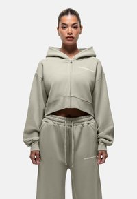 Felpa con zip accorciata e pantaloni abbinati in morbido tessuto verde chiaro. Presenta logo, vestibilità rilassata e cintura elastica.