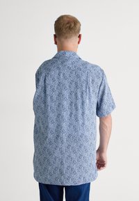 Chemise à manches courtes avec un motif tourbillonnant bleu et blanc, en tissu léger avec un col classique et une coupe droite.