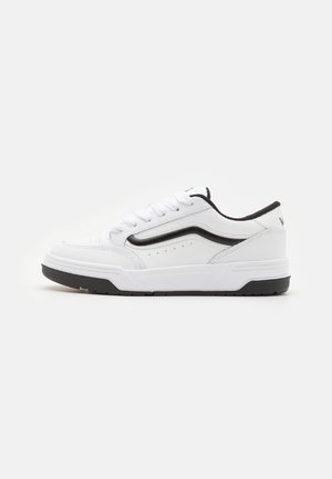 Sneakers bianchi a bassa cima con accenti neri, materiale simile alla pelle, punta rotonda e perforazioni ai lati per la traspirabilità. Suola in gomma nera.