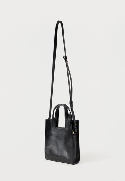 Μικρή μαύρη δερμάτινη τσάντα με δύο κοντά χερούλια και έναν μακρύ ρυθμιζόμενο ιμάντα ώμου, σε απλό φόντο.