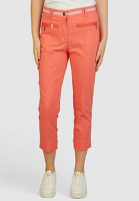 Koraalkleurige cropped pants met een zachte textuur, ritssluiting voorzakken en een witte gestreepte tailleband, gecombineerd met witte sneakers.