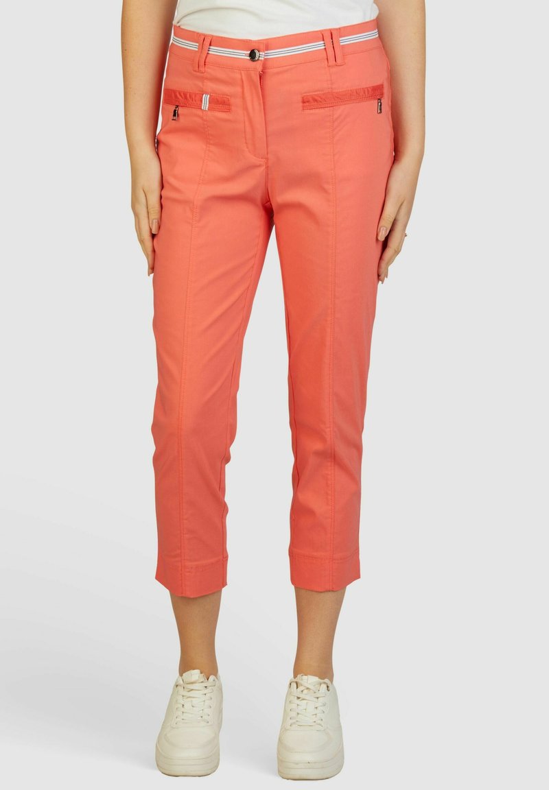Koraalkleurige cropped pants met een zachte textuur, ritssluiting voorzakken en een witte gestreepte tailleband, gecombineerd met witte sneakers.