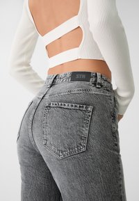 Högmidjade grå denimjeans med en blekt finish, med en svart midjebandsetikett och två bakfickor. Materialet har en texturerad look.