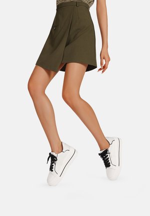 Gonna corta verde oliva con tasca frontale, abbinata a sneaker bianche con lacci neri e parte superiore testurizzata.