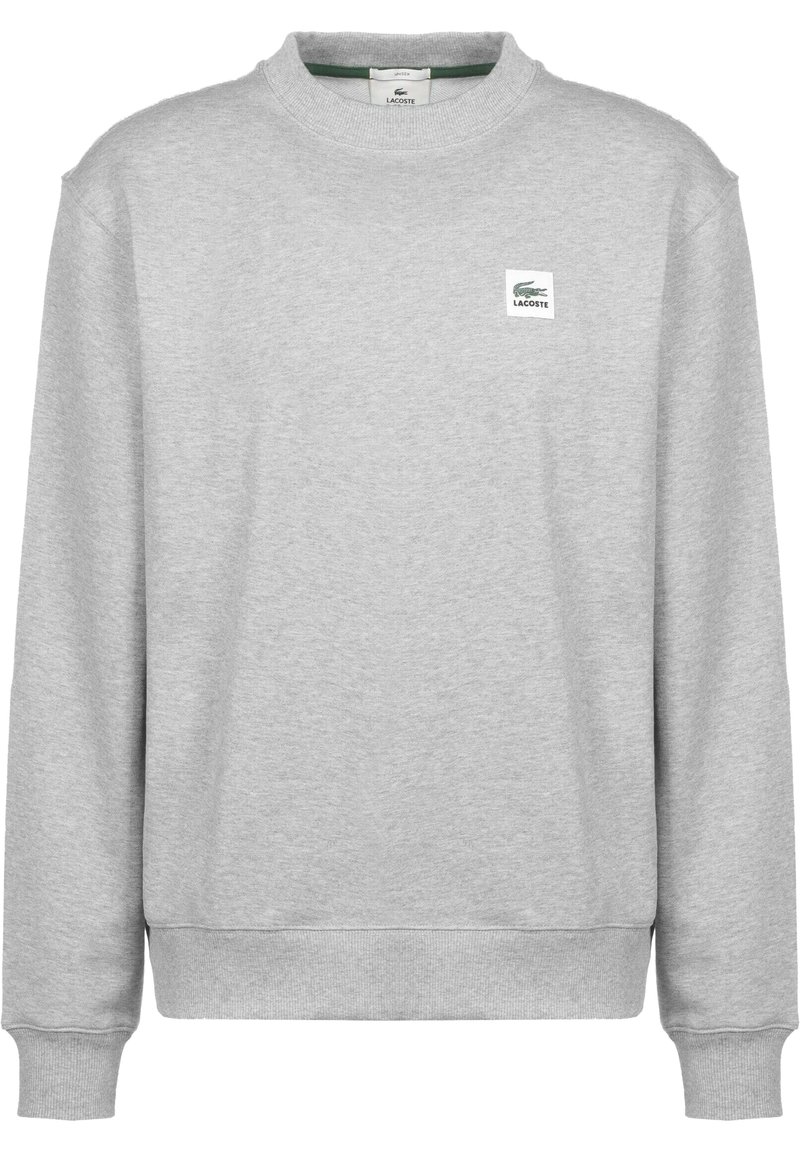 Felpa grigia con maniche lunghe, scollo a girocollo a coste e polsini elastici. Presenta una piccola toppa con il logo Lacoste sul davanti. Texture morbida.