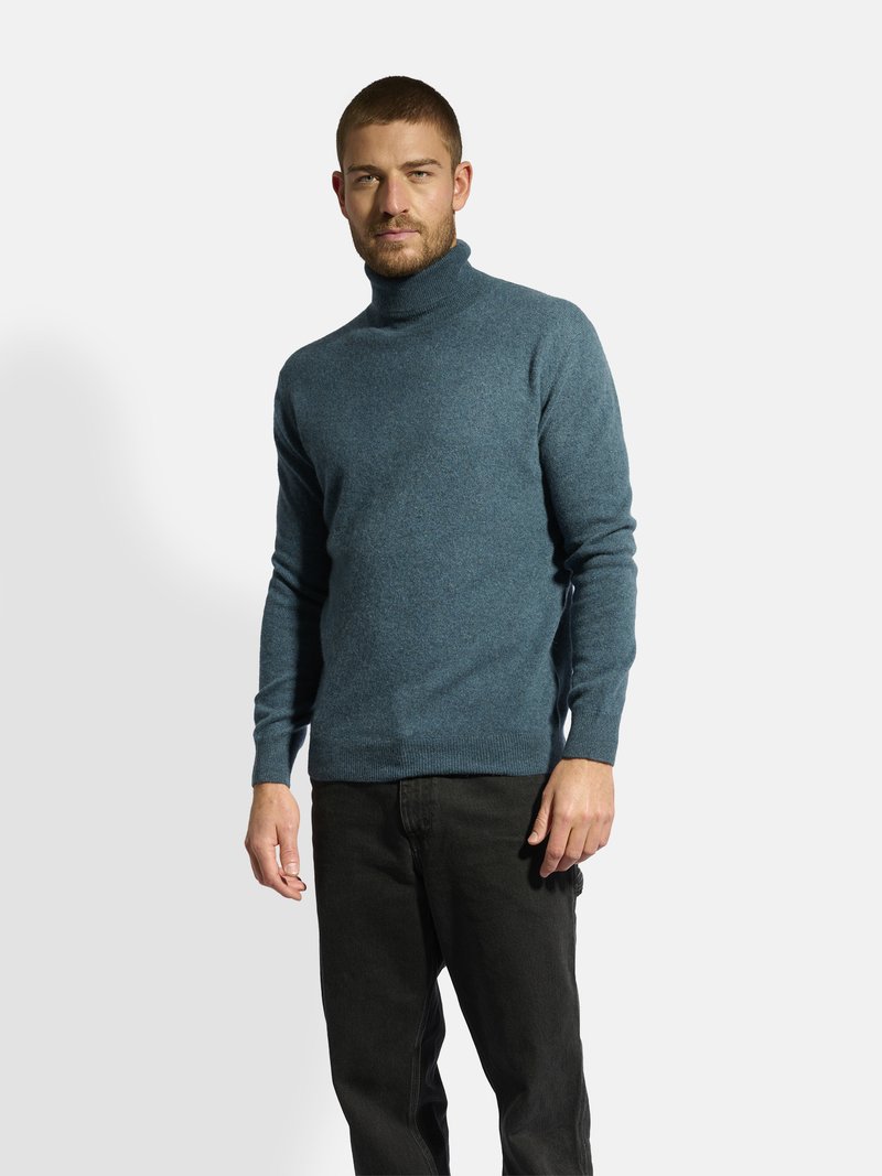 Blauer Rollkragenpullover aus gestricktem Material, mit einer taillierten Passform und gerippten Bündchen, kombiniert mit schwarzen Jeans.