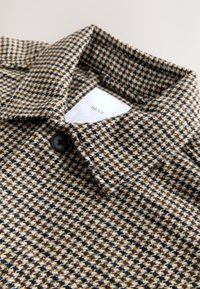 Cappotto di lana con un motivo a pied-de-poule, caratterizzato da una combinazione di colori marrone e nero, colletto con bottoni e un'etichetta contrassegnata "NEXT."