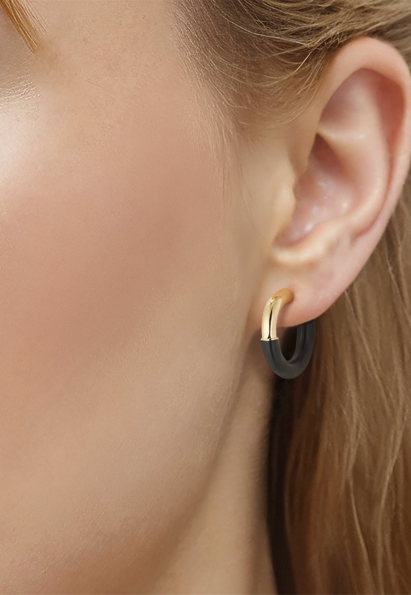 Close-up van iemands oor met een kleine oorring met half goud en half zwart ontwerp.
