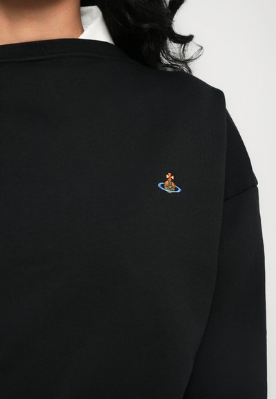 Svart hettegenser med rund hals. Har en liten, fargerik brodert båtlogo nær kragen. Glatt stoff uten synlig tekstur.