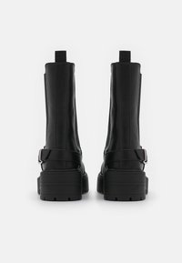 Botas de tobillo negras con plataforma, fabricadas en material sintético suave y con un diseño elegante, que cuentan con una correa de hebilla lateral y suelas texturizadas.