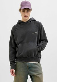 Dark gray hoodie made of soft fabric, featuring a kangaroo pocket, drawstring hood, and embroidered logo on the chest. Paired with light jeans.
