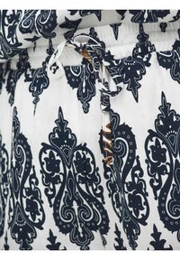 Tissu blanc avec des motifs floraux et cachemire noirs complexes, doté d'un cordon de serrage à la taille.