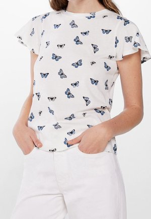 Top blanco de manga corta con mangas acampanadas con un patrón de mariposas azules y negras, combinado con pantalones blancos.