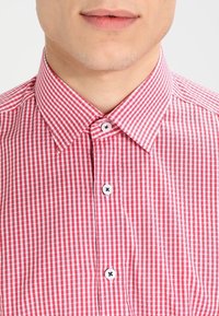 Camicia a quadri rossi e bianchi con un colletto piccolo, dotata di quattro bottoni bianchi con dettagli blu. Realizzata in un tessuto testurizzato.