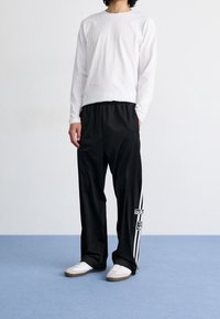 Svarta träningsbyxor med sidostripes och logotyp, kombinerade med en figurnära vit långärmad tröja och vita skor. Slät tyg med elastisk midjeband.