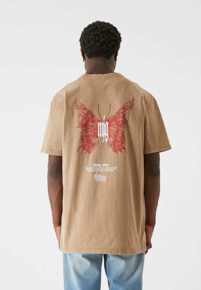 Brown cotton t-shirt featuring a large red butterfly design on the back, with white text underneath. Short sleeves and a relaxed fit.