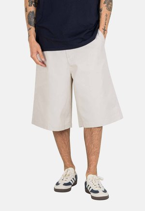 Light beige knee-length shorts made of cotton, featuring a relaxed fit, side pockets, and a straight leg design. Paired with white sneakers.
