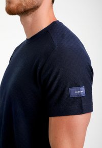 T-shirt in maglia a maniche corte blu navy con motivo testurizzato, colletto rotondo e un'etichetta sulla manica sinistra. Vestibilità classica e tessuto morbido.