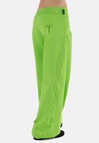 Groene, loszittende broek van zacht, rekbaar materiaal; heeft een brede tailleband en subtiele naden langs de zijkanten.