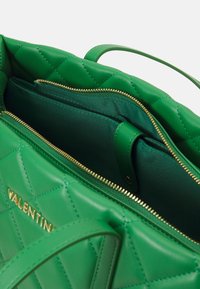 Kviltad grön läderhandväska med guldblixtlås och metalldelar. Interiören har tygfoder och flera fack för organisering.