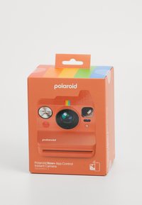 A Polaroid Now+ azonnali fényképezőgép élénk narancssárga csomagolása színes csíkokkal, lencsével, gombokkal és nyomtatott logóval. Függő füllel rendelkezik.