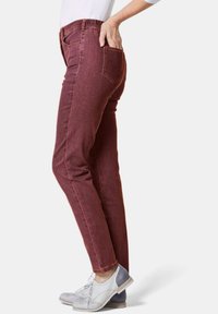 Jean bordeaux avec une coupe slim et une taille élastique, dotés de poches arrière et d'un ourlet classique. Associés à des chaussures grises et blanches.