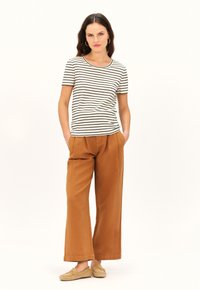 Camiseta de manga corta a rayas en color crema y negro, combinada con pantalones anchos en tono beige-marrón y zapatos estilo slip-on en color tostado. Diseño simple, corte relajado.