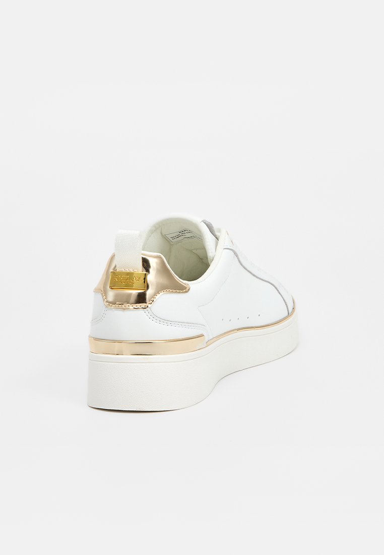 Baskets blanches à plateforme avec un accent en métal doré sur le talon et une languette, couture visible, et texture en cuir lisse sur fond uni.