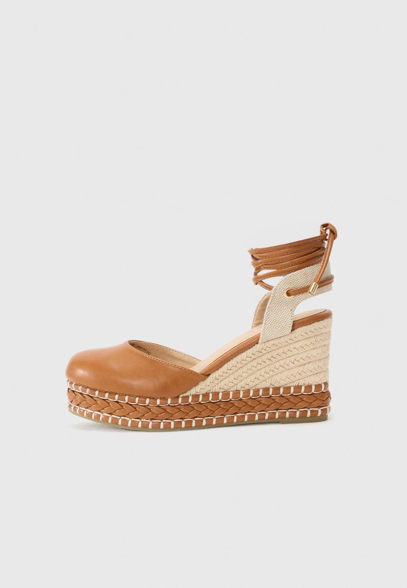 Espadrille de cuero marrón con tacón de yute trenzado, que cuenta con un detalle trenzado, una tira elástica en el tobillo y una punta redondeada suave.