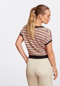 Kurzärmliges, gestreiftes Strickoberteil mit lebhaften Farben, einem schwarzen Rippabschluss und strukturiertem Material. Kombiniert mit beigen, hochtaillierten Hosen.